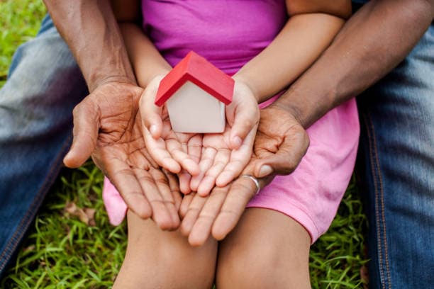 Family hands holding a small model house, representing safe and stable housing